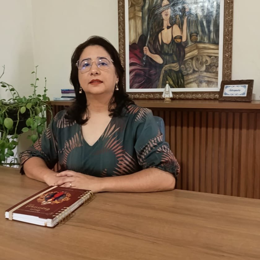 Dra. Íris Souto Maior em sua mesa de trabalho, com um quadro da Justiça ao fundo